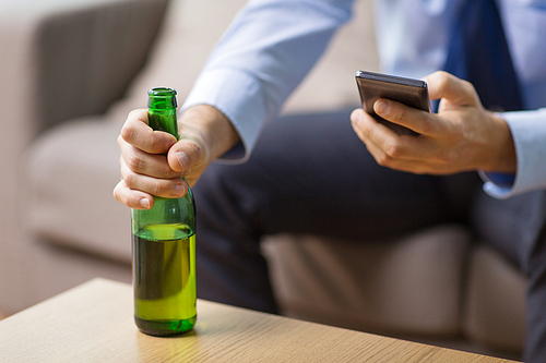 alcoholism, alcohol addiction and people concept - close up of man with smartphone drinking bottled beer