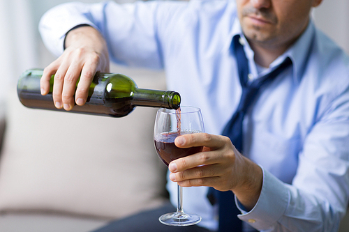 alcoholism, alcohol addiction and people concept - male alcoholic pouring red wine to glass at home