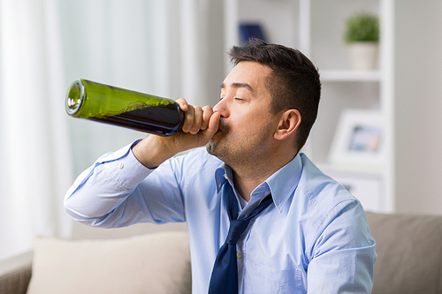 alcoholism, alcohol addiction and people concept - male alcoholic drinking red wine from bottle neck at home