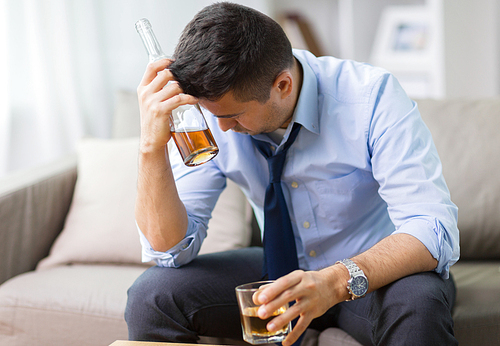 alcoholism, alcohol addiction and people concept - male alcoholic with bottle and glass drinking whiskey at home