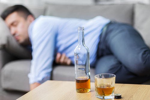 alcoholism, alcohol addiction and people concept - bottle with glass of whiskey on table and sleeping drunk man