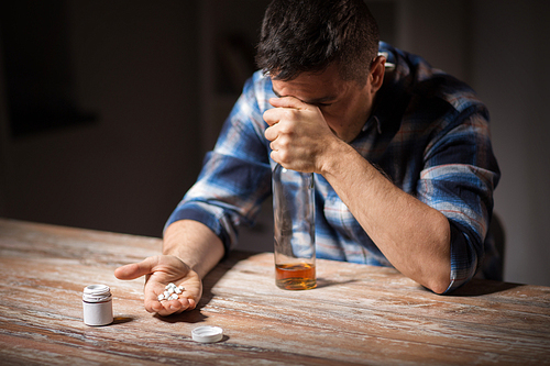 depression, drug abuse and addiction people concept - unhappy drunk man with bottle of alcohol and pills committing suicide by overdosing on medication at night