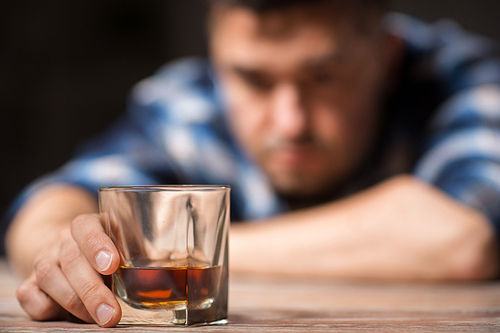 alcoholism, alcohol addiction and people concept - male alcoholic with glass of whiskey lying on table at night