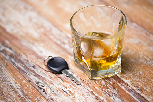 alcohol abuse, drunk driving and people concept - close up of whiskey glass and car key on table