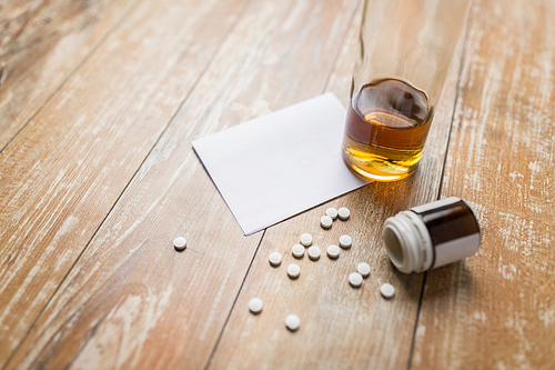 drug abuse, addiction and suicide concept - bottle of alcohol and pills on table