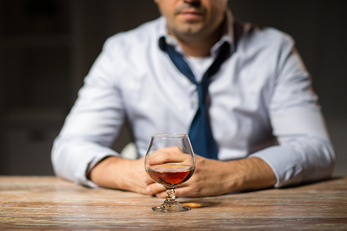 alcoholism, alcohol addiction and people concept - male alcoholic drinking brandy on table at night