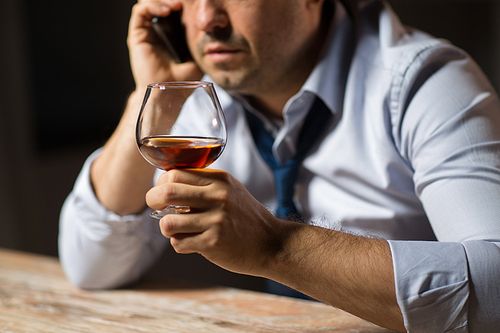alcoholism, alcohol addiction and people concept - close up of male alcoholic drinking brandy and calling on smartphone at night