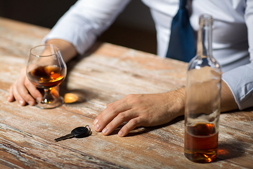 alcohol abuse, drunk driving and people concept - close up of male driver hands with brandy glass and car key on table at night