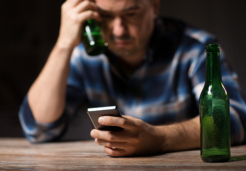 alcoholism, alcohol addiction and people concept - drunk man with smartphone and bottle of beer at night