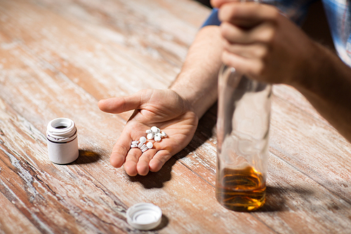 depression, drug abuse and addiction people concept - unhappy drunk man with bottle of alcohol and pills committing suicide by overdosing on medication at night