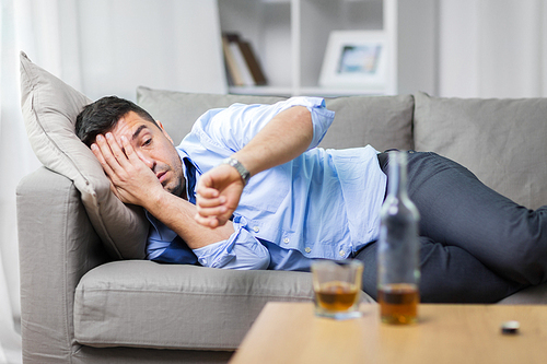 alcoholism, alcohol addiction and people concept - male alcoholic lying on sofa and looking at wristwatch