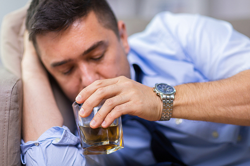 alcoholism, alcohol addiction and people concept - close up of male alcoholic lying on sofa and drinking whiskey
