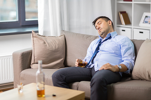 alcoholism, alcohol addiction and people concept - male alcoholic with glass of whiskey sleeping on sofa at home