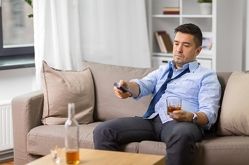 alcoholism, alcohol addiction and people concept - drunk man or alcoholic with tv remote drinking whiskey at home