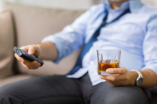 alcoholism, alcohol addiction and people concept - close up of man with tv remote drinking whiskey at home