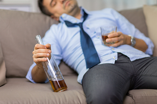 alcoholism, alcohol addiction and people concept - close up of man sleeping with bottle of whiskey on sofa at home