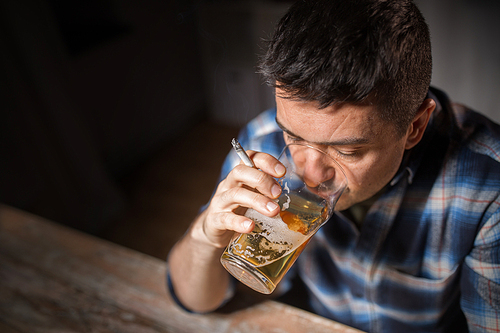 alcoholism, alcohol addiction and people concept - close up of male alcoholic drinking beer and smoking cigarette at night
