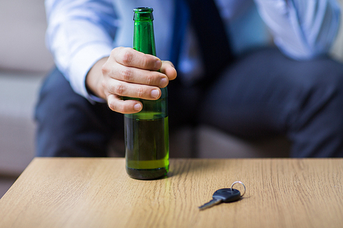 alcohol abuse, drunk driving and people concept - close up of male driver hand with beer bottle and car key on table