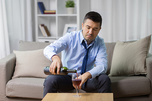 alcoholism, alcohol addiction and people concept - male alcoholic pouring red wine to glass at home