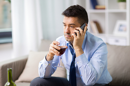 alcoholism, alcohol addiction and people concept - male alcoholic drinking wine and calling on smartphone at home