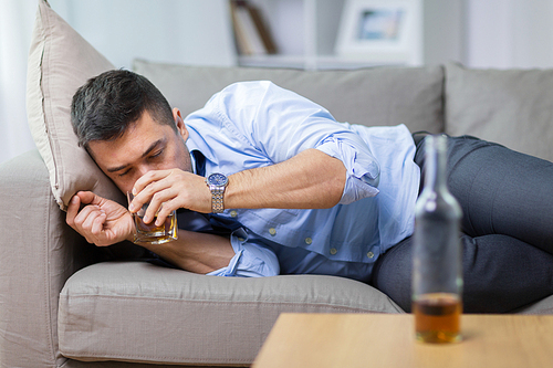 alcoholism, alcohol addiction and people concept - male alcoholic lying on sofa and drinking whiskey
