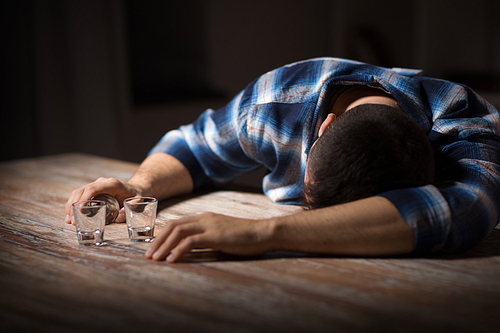 alcoholism, alcohol addiction and people concept - male alcoholic with empty glasses lying or sleeping on table at night