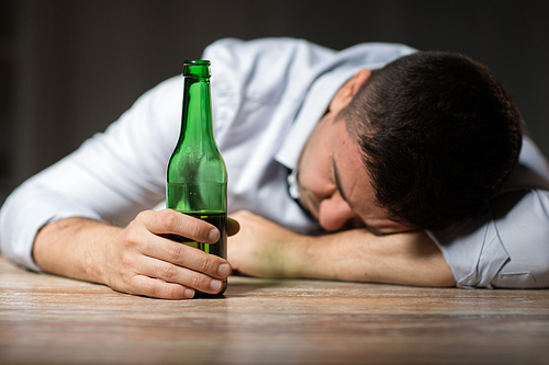 alcoholism, alcohol addiction and people concept - male alcoholic with beer bottle lying or sleeping on table at night