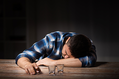 alcoholism, alcohol addiction and people concept - male alcoholic with empty glasses lying or sleeping on table at night