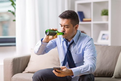 alcoholism, alcohol addiction and people concept - male alcoholic with smartphone drinking bottled beer at home