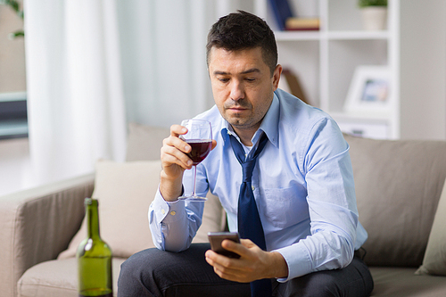 alcoholism, alcohol addiction and people concept - drunk man with smartphone and bottle of wine at home