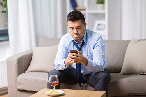 alcoholism, alcohol addiction and people concept - drunk man with smartphone and glass of brandy at home