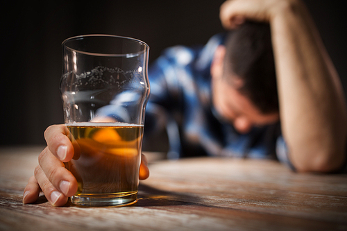 alcoholism, alcohol addiction and people concept - male alcoholic with glass of beer lying or sleeping on table at night