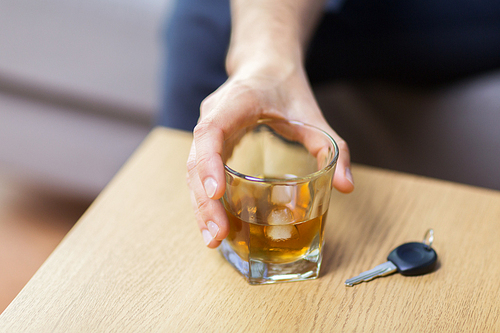 alcohol abuse, drunk driving and people concept - close up of male driver hand with whiskey glass and car key on table