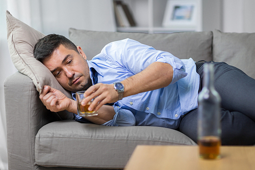 alcoholism, alcohol addiction and people concept - male alcoholic lying on sofa and drinking whiskey