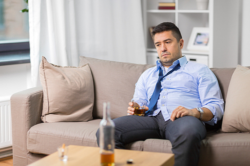 alcoholism, alcohol addiction and people concept - male alcoholic with glass drinking whiskey at home