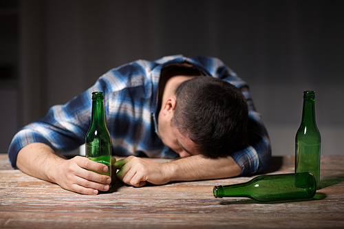 alcoholism, alcohol addiction and people concept - male alcoholic with beer bottles lying or sleeping on table at night