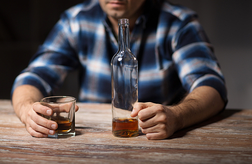 alcoholism, alcohol addiction and people concept - male alcoholic with bottle and glass drinking whiskey at night