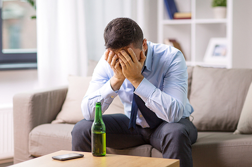 alcoholism, alcohol addiction and people concept - male alcoholic with bottle of beer at home