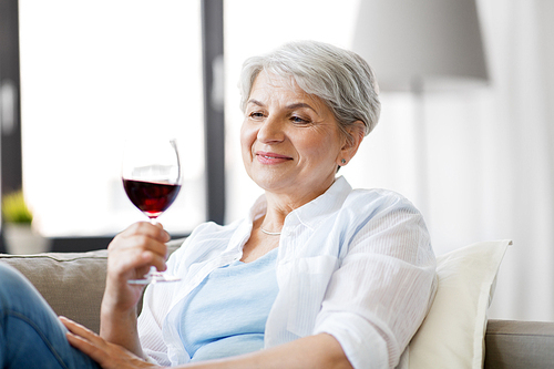 people, alcohol and leisure concept - happy smiling senior woman with glass of red wine at home