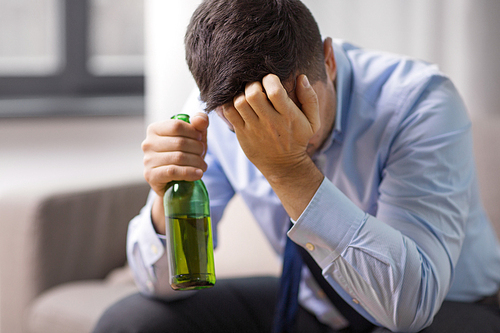 alcoholism, alcohol addiction and people concept - male alcoholic drinking beer from bottle at home