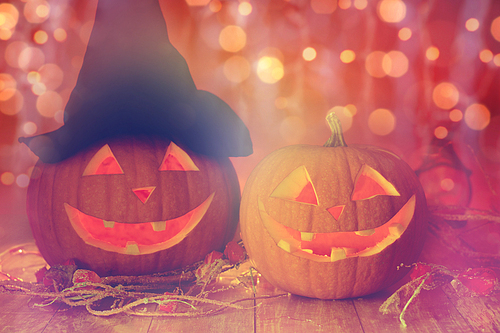 holidays, halloween and decoration concept - close up of carved pumpkins with smiley faces and witch hat on table over lights