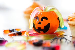 halloween, junk food and confectionery concept concept - multicolored gummy worms and candies with jack-o-lantern decoration on table