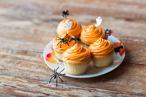 food, baking and holidays concept - cupcakes or muffins and candies with halloween party decorations on wooden table