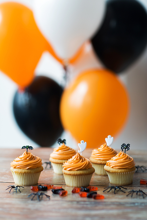 food, baking and holidays concept - cupcakes or muffins and candies with halloween party decorations on wooden table