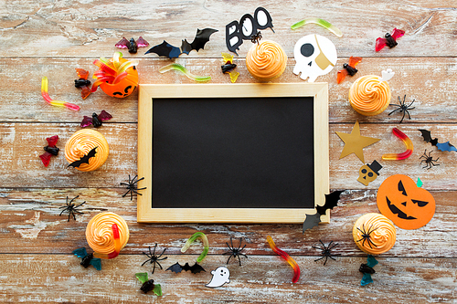 holidays, school and party concept - halloween decorations and treats with blank chalkboard on wooden boards background