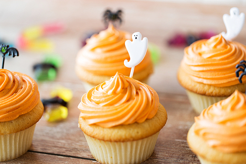 food, baking and holidays concept - cupcakes or muffins and candies with halloween party decorations on wooden table