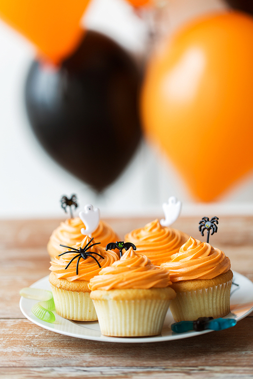 food, baking and holidays concept - cupcakes or muffins with halloween party decorations on wooden table