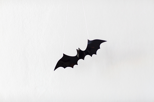 halloween, decoration and scary concept - black flying bat hanging on strings over white background