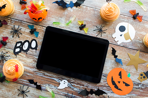 holidays, technology and party concept - halloween decorations and treats with tablet pc computer on wooden boards background