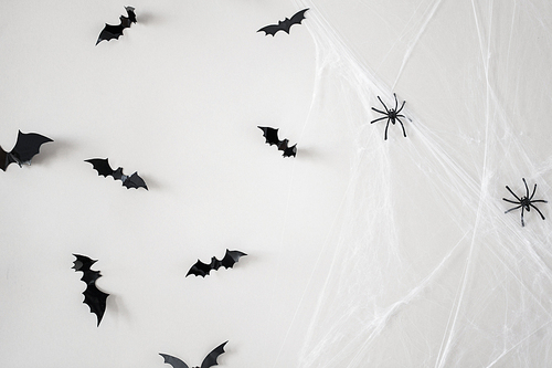 halloween, decoration and scary concept - black flying bats and spiders on web over white background